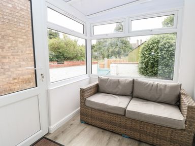 A sunroom with a rattan sofa with gray cushions and windows showing an outdoor garden area