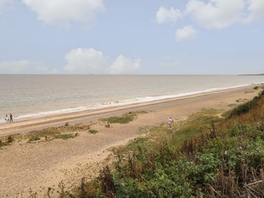 A beach with sand, pebbles, sparse vegetation and people walking near the shore at Sole Bay Cottage in Lowestoft