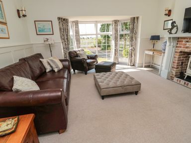 A living room with leather sofa armchair ottoman fireplace and large window at 9 Station Cottages in Belford