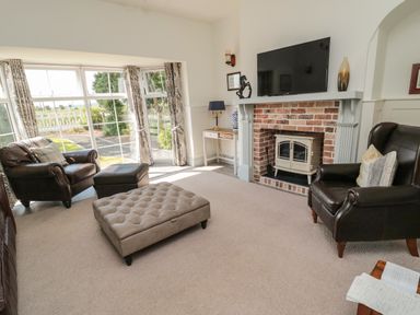 A living room with leather armchairs a television above a brick fireplace and large windows at 9 Station Cottages in Belford