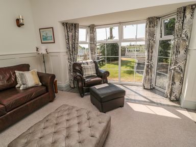 A living room with a leather sofa and armchair by bay windows with patterned curtains at 9 Station Cottages in Belford