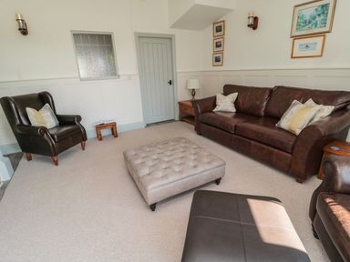A living room with brown leather sofas a tufted ottoman and framed pictures on walls at 9 Station Cottages in Belford