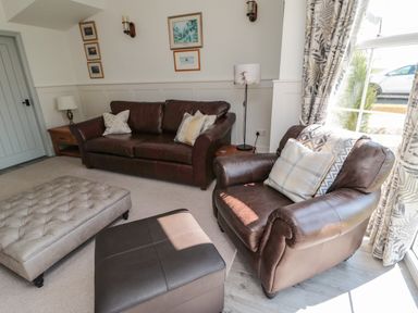 A living room with a brown leather sofa and armchair with cushions and two ottomans near a window at 9 Station Cottages Belford