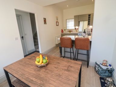 A kitchen with a wooden table holding a fruit bowl brown bar stools at the counter and pet food supplies in a corner at 9 Station Cottages in Belford