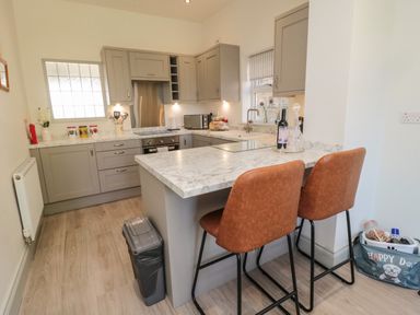 A kitchen with gray cabinets marble countertops two brown bar stools and kitchen appliances at 9 Station Cottages in Belford