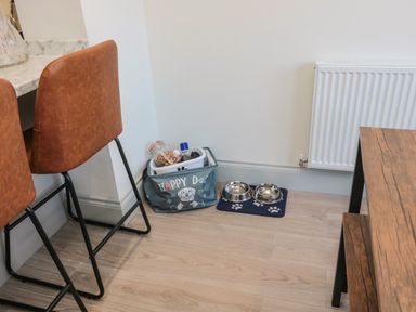 A corner of a kitchen with two brown chairs a wooden table a dog food station with bowls and a container at 9 Station Cottages in Belford