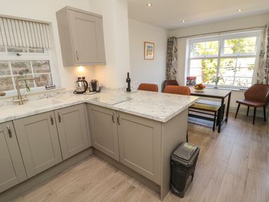 A kitchen with marble countertops, beige cabinets, a dining table with chairs, and large windows at 9 Station Cottages in Belford