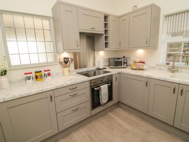 A kitchen with grey cabinets a stove a microwave and utensils at 9 Station Cottages in Belford