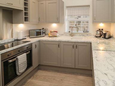 A kitchen with gray cabinets marble countertops an oven microwave toaster kettle and a window with a striped blind at 9 Station Cottages in Belford