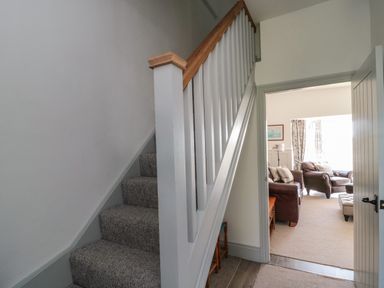 A stairway with carpeted steps and a wooden handrail leading to a living room with sofas and a window at 9 Station Cottages in Belford