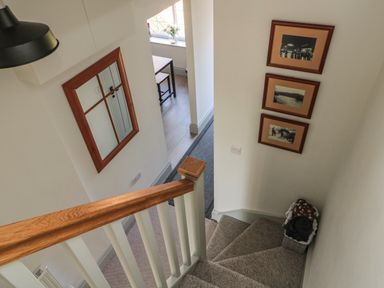 A staircase with carpeted steps leading down to a hallway with framed pictures on the wall and a mirror on another wall at 9 Station Cottages in Belford
