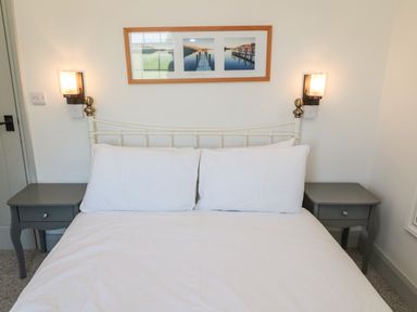 A bed with white bedding flanked by two gray nightstands and wall lamps in a bedroom at 9 Station Cottages in Belford