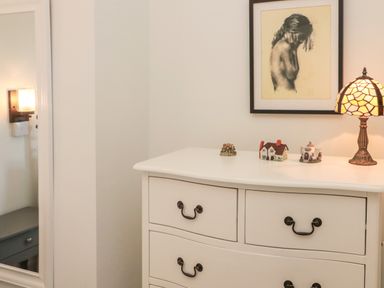A white dresser with four drawers holding small decorative houses and a lamp beside a framed sketch in a room at 9 Station Cottages in Belford
