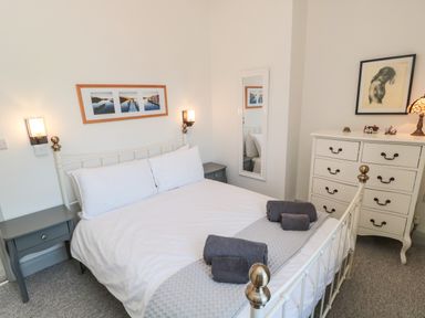 A bedroom with a white metal bed, gray bedside tables, folded towels on the bed, a white chest of drawers with a lamp and framed artwork at 9 Station Cottages in Belford