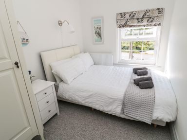 A bedroom with a white bed a bedside table and a window with patterned blind at 9 Station Cottages in Belford