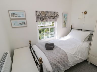 A bedroom with a single bed with white bedding and grey throw near a window with patterned roman blind at 9 Station Cottages in Belford
