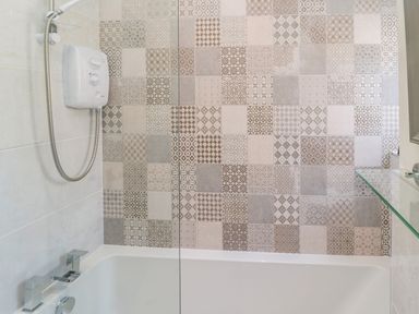 A bathroom with a bathtub and a shower with patterned tiles on the wall at 9 Station Cottages in Belford
