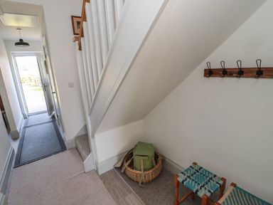 A hallway with an open door a stairway and a basket with a green bag and two small stools at 9 Station Cottages in Belford