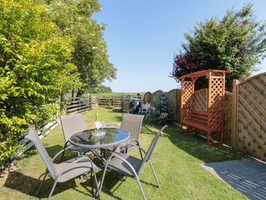 A garden with a glass table and four chairs and a wooden bench under a lattice arch at 9 Station Cottages in Belford