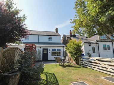 An outdoor garden area with a table and chairs in front of white houses with a wooden fence and trees at 9 Station Cottages in Belford