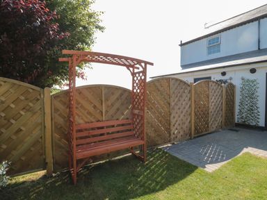 A wooden bench with a lattice backrest and overhead frame in a garden next to a wooden fence at 9 Station Cottages in Belford