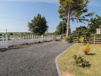 A gravel driveway beside a lawn with small shrubs and trees near a white picket fence and wooden fence at 9 Station Cottages in Belford