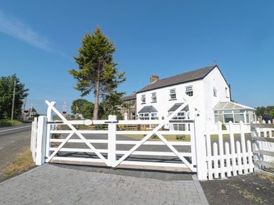 A white house with a conservatory behind a white wooden gate at 9 Station Cottages in Belford