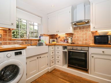 A kitchen with a washing machine a sink an oven microwave and white cabinets at Barton Cottage in Bourton-On-The-Water