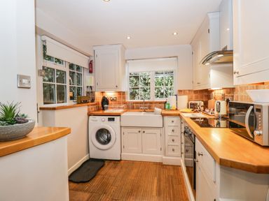 A kitchen with wooden countertops white cabinets a washing machine and appliances at Barton Cottage Bourton-On-The-Water