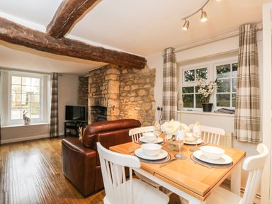 A dining table set with plates and bowls next to a living area with a leather sofa and a stone fireplace at Barton Cottage in Bourton-On-The-Water