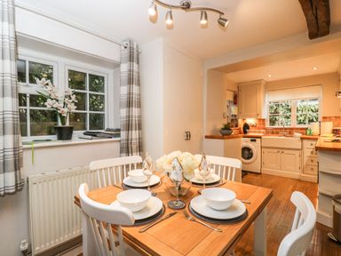 A dining table set for four next to a window and an open kitchen in a home at Barton Cottage in Bourton-On-The-Water