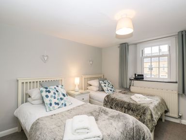 A bedroom with two single beds with fur throws and patterned cushions with a window on the side at Barton Cottage in Bourton-On-The-Water