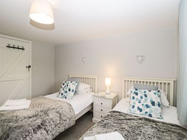 A bedroom with two single beds a bedside table with a lamp and heart decorations on the wall at Barton Cottage in Bourton-On-The-Water