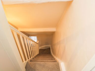 A carpeted staircase with white wooden railing and beige walls at Barton Cottage in Bourton-On-The-Water