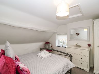 A bedroom with a bed a chair a chest of drawers a wardrobe and a window at Barton Cottage in Bourton-On-The-Water