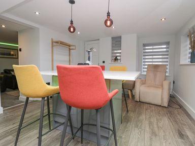 A room with a table surrounded by colorful chairs and a beige recliner chair near windows at Crag View Cottage in Stainton with Adgarley near Dalton-In-Furness