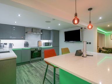 A modern kitchen with grey cabinets a white countertop a mounted television and colored chairs at Crag View Cottage in Stainton with Adgarley near Dalton-In-Furness
