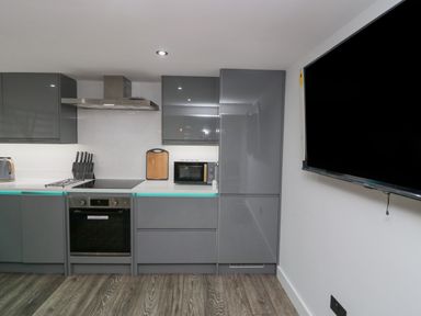 A kitchen with grey cabinets an oven a microwave a cutting board and a wall mounted television at Crag View Cottage in Stainton with Adgarley near Dalton In Furness