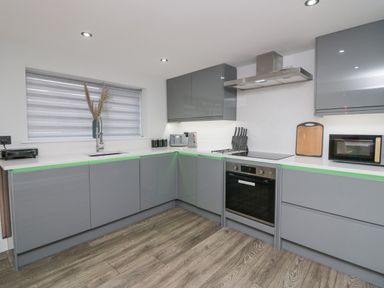 A kitchen with gray cabinets a built-in oven a stovetop knives a microwave and a window with blinds at Crag View Cottage in Stainton with Adgarley near Dalton-In-Furness