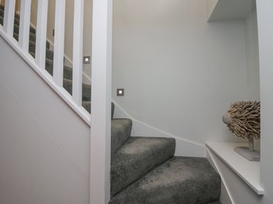 A carpeted staircase with white railings and a small decorative wooden sculpture on a shelf at Crag View Cottage in Stainton with Adgarley near Dalton-In-Furness