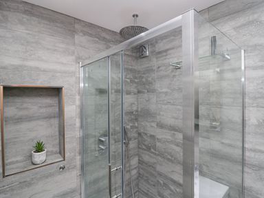 A shower area with glass doors and grey tiled walls with a small plant in a recessed shelf at Crag View Cottage in Stainton with Adgarley near Dalton-In-Furness