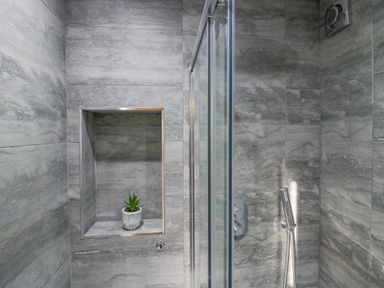 A shower area with grey tiled walls a built-in shelf with a small plant and a handheld showerhead Crag View Cottage Stainton with Adgarley near Dalton-In-Furness