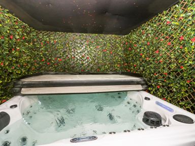 An indoor hot tub with water jets surrounded by walls covered in green leaves with red flowers at Crag View Cottage in Stainton with Adgarley near Dalton-In-Furness