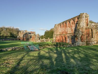 Ruins of old stone buildings with arched windows and green grass surrounded by trees at Crag View Cottage in Stainton with Adgarley near Dalton-In-Furness