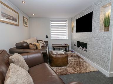 A living room with brown leather sofas a wall-mounted television a fireplace and a window with striped blinds at Crag View Cottage in Stainton with Adgarley near Dalton-In-Furness