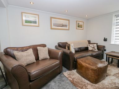 A living room with brown leather sofas, an ottoman, framed pictures on the wall, and nested side tables at Crag View Cottage in Stainton with Adgarley near Dalton-In-Furness
