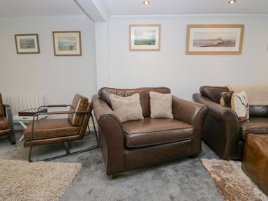 A living room with leather armchairs and a sofa with cushions on a carpet with framed pictures on the wall at Crag View Cottage in Stainton with Adgarley near Dalton-In-Furness