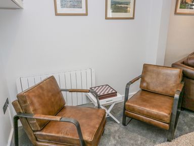 Two brown leather chairs with a white side table and a chessboard in a room at Crag View Cottage in Stainton with Adgarley near Dalton-In-Furness