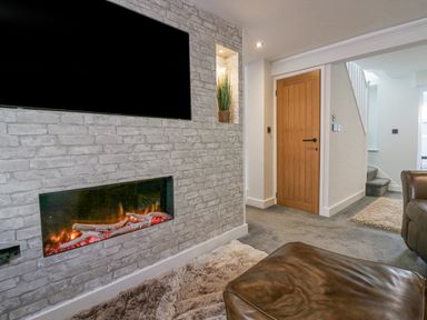 A living room with a wall-mounted television and a fireplace next to a wooden door and staircase at Crag View Cottage in Stainton with Adgarley near Dalton-In-Furness