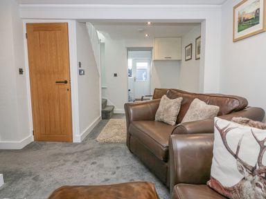 A living room with brown leather sofas and a wooden door at Crag View Cottage in Stainton with Adgarley near Dalton-In-Furness